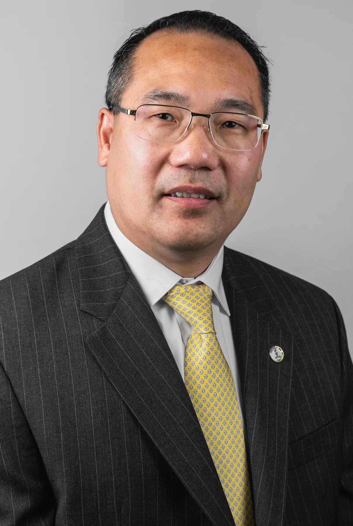 Executive male headshot in a dark suit and yellow tie