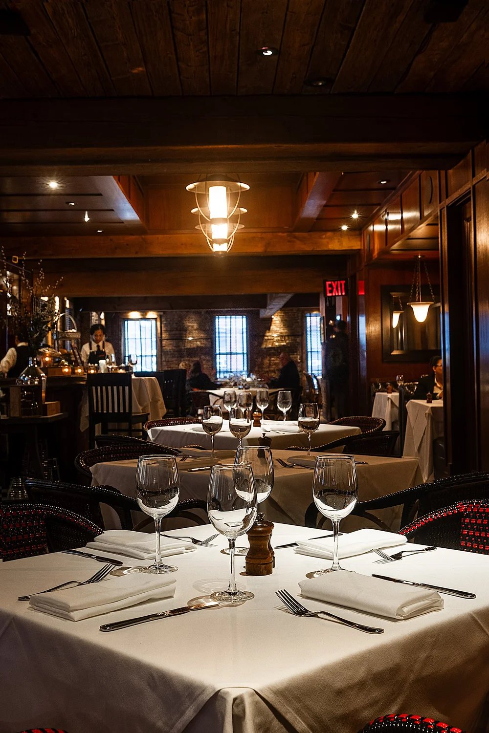 PJ Clarke's dining room with a reclaimed wood ceiling, brick walls and white linen tables